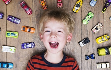 young boy laying down on floor with cars around him
