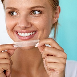 A smiling woman using teeth whitening strips 
