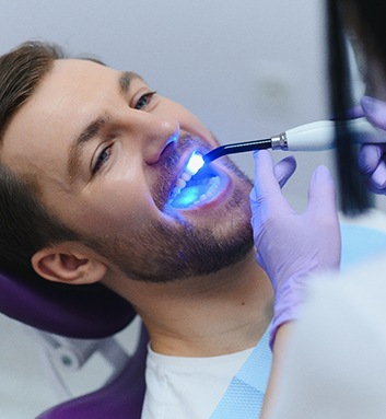 Dentist applying UV light to man&rsquo;s dental bonding
