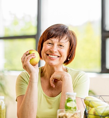 woman sitting at a table and holding an apple